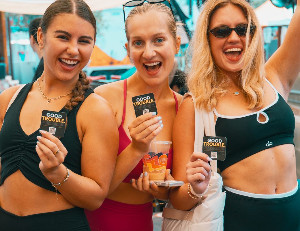 Three friends holding Good Trouble ATX cards at an event